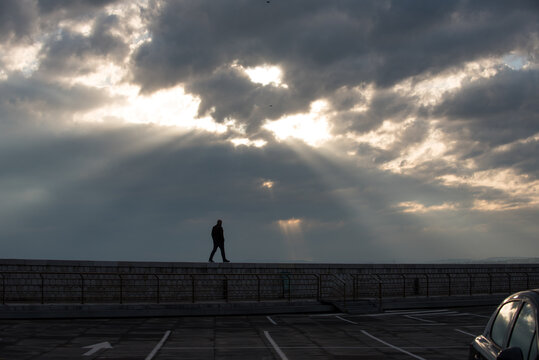 silhouette d'un homme vu de loin marchant confiant sur un mur et sous un ciel nuageux perc&eacute; de rayons de soleil entourant la silhouette de fa&ccedil;on pyramidale 