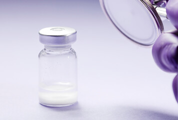 glass and aluminum vaccine bottle, stethoscope in the air, with . Soft lilac background