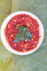 Chili paste in a small bowl with a parsley leaf on a large leaf plating