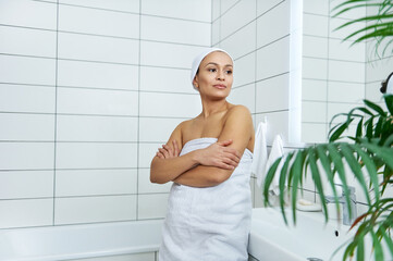 Young woman stands in the middle of the bathroom with her arms folded on her chest