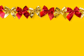 horizontal festive background: shiny red and gold bows on a yellow background - flat lay. Copy...