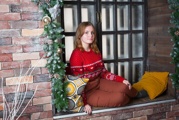 A blonde girl in a red sweater sits on the windowsill.
