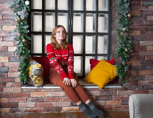 A blonde girl in a red sweater sits on the windowsill.