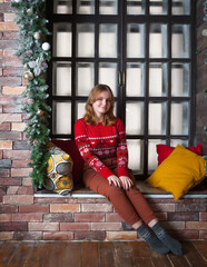 A blonde girl in a red sweater sits on the windowsill.