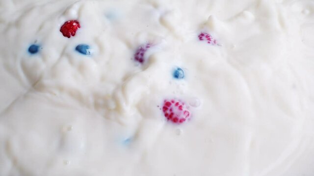 Blueberries and raspberries falling into milk in slow motion