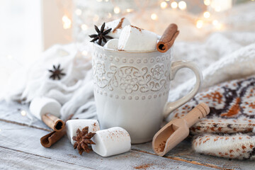 Winter hot drink. Cozy home composition with white mug with chocolate and marshmallow, cinnamon. Knitted mittens, christmas lights, wooden background. Festive holiday atmosphere, family spirit. Close