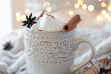 Winter hot drink. Cozy home composition with white mug with chocolate and marshmallow, cinnamon. Knitted mittens, christmas lights, wooden background. Festive holiday atmosphere, family spirit. Close