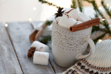 Winter hot drink. Cozy home composition with white mug with chocolate and marshmallow, cinnamon. Knitted mittens, christmas lights, wooden background. Festive holiday atmosphere, family spirit. Close
