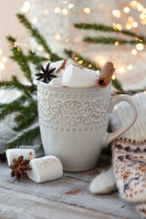 Winter hot drink. Cozy home composition with white mug with chocolate and marshmallow, cinnamon. Knitted mittens, christmas lights, wooden background. Festive holiday atmosphere, family spirit. Close