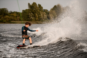 young athletic man holding taut rope and rides down on wave on wakeboard