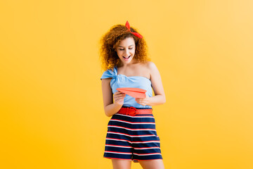 smiling young woman in summer outfit holding paper plane on yellow