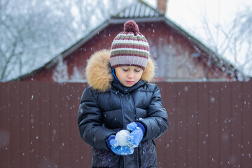 little boy sculpts snowballs in the village yard, a boy plays snowballs, snow falls