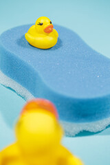 Small and large yellow rubber duck on top of blue bath sponge, on blue background