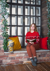 A blonde girl in a red sweater sits on the windowsill.