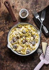 Pork sausage and cream sauce fettuccine pasta  in a frying pan on a wooden background, top view