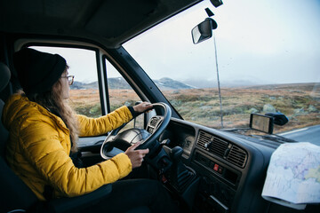 Young woman drive camping van on epic mountain road. Female adventurer travel in remote locations to camping destination. Vanlife lifestyle for urban travellers 