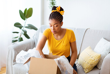 Frustrated black lady unpacking wrong parcel, delivery mistake