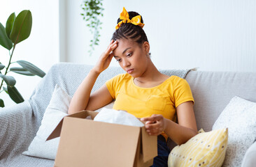 Sad young lady unpacking wrong parcel, delivery mistake