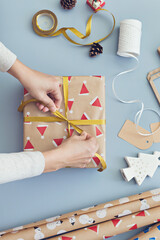 Preparing for Christmas holidays. Female hands wrapping Christmas gift box, background with Christmas ornament and decor.
