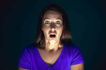 Extreme. Portrait of young crazy scared and shocked caucasian woman isolated on dark background. Copyspace for ad. Bright facial expression, human emotions concept. Looking horror on TV, cinema.