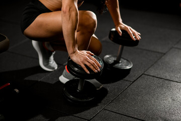 muscular arms of woman leans on dumbbells that lie on the floor