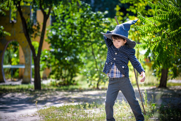 Toddler boy in pointed hat playing with magic wand outdoors. Little wizard. Halloween concept