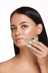 Beautiful girl with natural makeup and clean skin. Holds in hand a jade face scrubber for slimming anti aging wrinkles. Massage instrument for body skin care. Detox facial massager