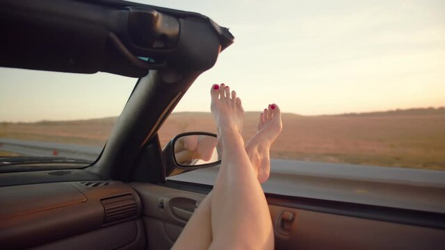 Two beautiful, slender woman's legs protrude from the front window of the cabriolet. Toenails arae painted red. Concept of recreation ,travel by car.