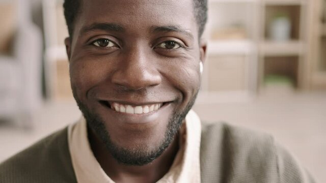 Close up of face of young African-American businessman wearing wireless headphone in his ear looking at camera and smiling
