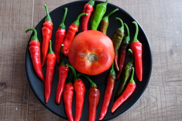 Red vegetables on a black plate. Organic tomatoes with peppers on wooden background. Summer or autumn concept. Natural food. It is called "Kirmizi Biber" and "Domates" in Turkish.