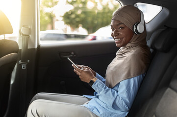 Happy Black Muslim Lady Enjoying Car Trip With Smartphone And Wireless Headphones