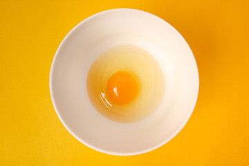 Egg with yolk in a bowl on a yellow background. Minimalist concept of cooking