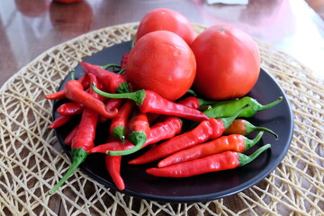 Red vegetables on a black plate. Organic tomatoes with peppers on wooden background. Summer or autumn concept. Natural food. It is called 