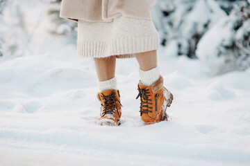 Warm brown winter boots. A girl in shoes stands in the snow. Stylish winter clothes for long walks