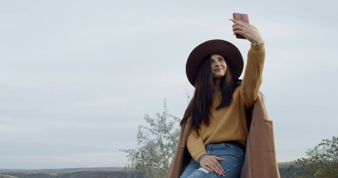 a girl with a hat and coat takes selfie pictures with the phone outside.
