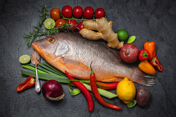 Raw Red snapper fish with spices and herbs ingredients for cooking on dark background., top view