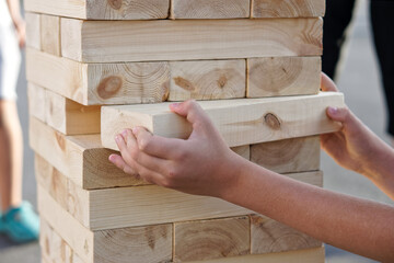 The hands of a child taking one block from a tower during a street game of giant Jenga. Outside the...