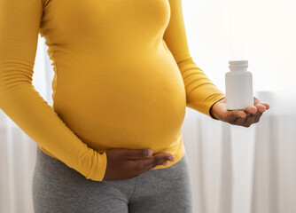 Unrecognizable black pregnant woman holding white jar with pills