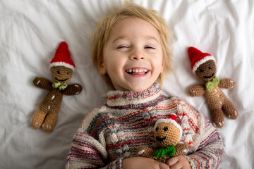 Cute toddler child, holding knitted toy, sitting in bed, playing with pet dog