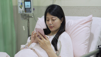 Obraz na płótnie Canvas sickness asian woman seated on hospital bed is smiling while looking at heartfelt messages about cheering her up on her social networking page.