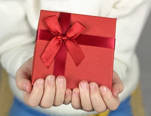 Foto auf Acrylglas Nahaufnahme von Kinderhänden schenken eine kleine Geschenkbox, die mit rotem Band und Schleife umwickelt ist. © Albert Ziganshin