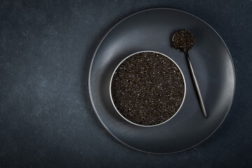 Bowl of black caviar of sturgeon fish on a dark blue background.View from above