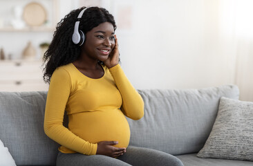 Happy pregnant black woman listening to music in headphones