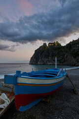 Fototapeta na wymiar A typical wooden fishing boat at the beach under the illuminated Rocca, near Taormina in long exposure.