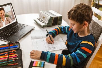 Little boy writes musical notes and violin key at home online course on laptop.Online training,...