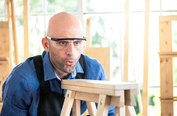 Carpenter workers wear safety glasses and blowing wood chips from the workpiece in the modern wood...