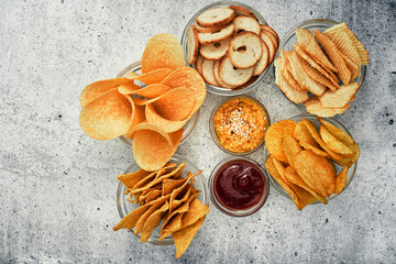 Potato and corn chips, snacks, crackers in transparent glass plates and sauces. Mix of snacks.