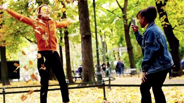 Two happy girlfriends taking photo with golden leaves in autumn park, 120fps
