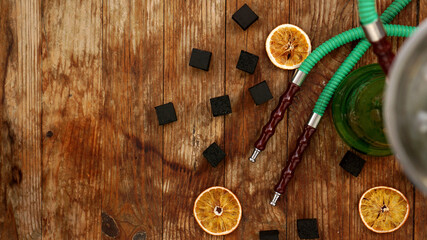 Coals for hookah on wooden background with dry oranges and hookah pipes. Place for text