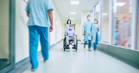 Ill senior man with protective safety mask on face in a wheelchair and a confident doctor in the medical mask while transporting on the hospital.